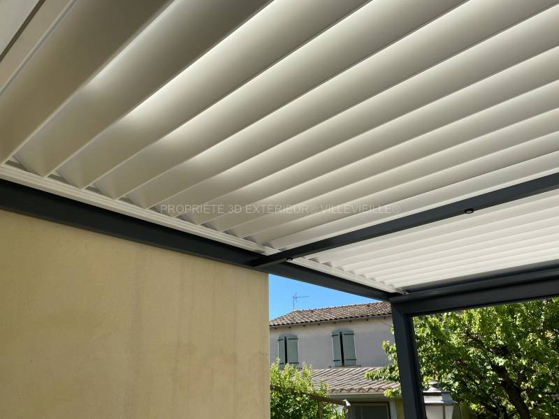 Pergola bioclimatique adossée sur deux murs en aluminium avec un déporté grande résistance intempéries bi coloration structure gris anthracite (Ral 7016) lames orientables double parois blanche (Ral 9010) installée sur la commune Le Cailar dans le départe